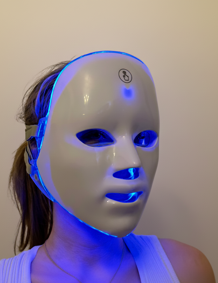 Person wearing a LED face mask with blue light on a plain background