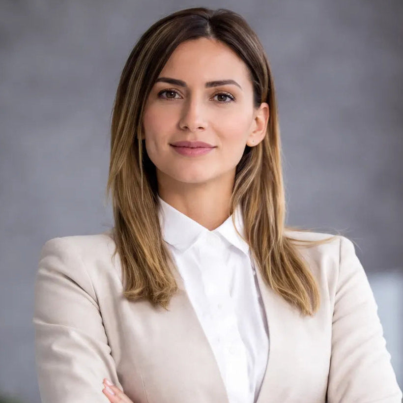 Woman in a beige blazer and white shirt standing against a gray background