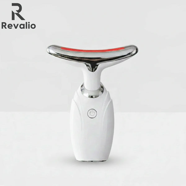 Front view of the white Revalio LED Facial Neck Massager standing upright against a white and grey background.