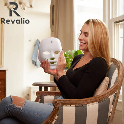 Woman holding the Revalio Health LED  face mask in a home setting with Revalio branding.