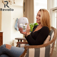 Woman holding the Revalio Health LED  face mask in a home setting with Revalio branding.