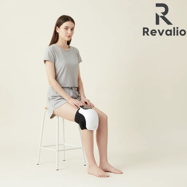 Woman using the Revalio Smart Knee Massager With Heat while sitting on a stool with Revalio logo in the corner.